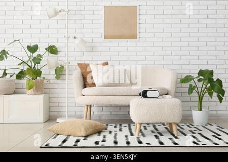 Modern living room interior with virtual reality headset, cozy sofa, potted plants, and white brick wall Stock Photo
