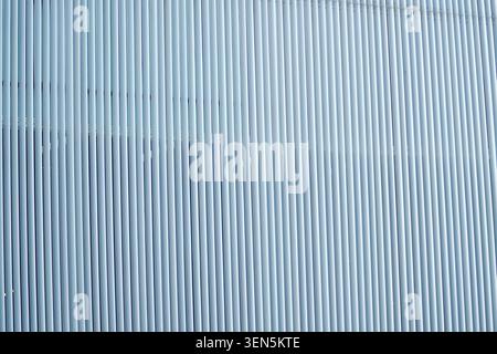 A textured wall made of vertical blue lines stands in an urban environment. Soft daylight casts subtle shadows, enhancing the wall's design. The scene Stock Photo