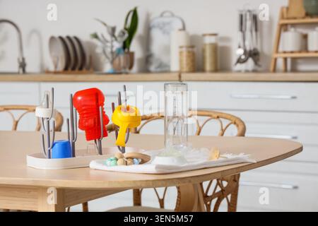 Baby bottle drying rack with colorful accessories, measuring cup, pacifier, and wooden teether on a kitchen table Stock Photo