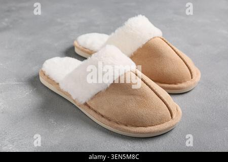 Comfortable beige suede slippers with white faux fur lining on gray concrete background for home relaxation, the soft indoor footwear provides warmth Stock Photo