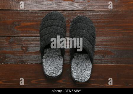 Comfortable gray house slippers with faux fur lining on dark brown wooden floor for relaxation and home comfort, this footwear is suitable for home us Stock Photo