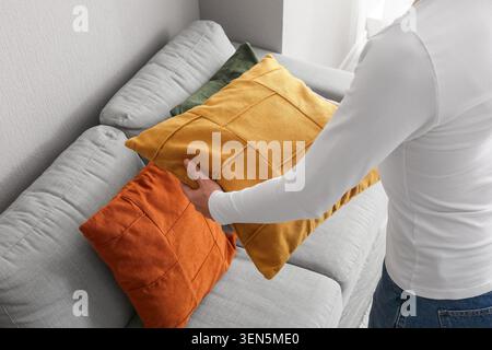 Person arranging decorative pillows on a modern gray sofa, home interior design and comfort Stock Photo