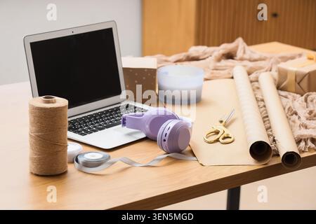 Creative workspace with laptop, craft supplies, and headphones on wooden table for online business and DIY projects Stock Photo