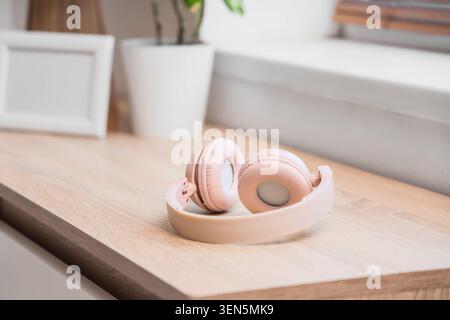 Pink wireless headphones on wooden desk, modern audio technology for music and podcasts, home office entertainment device Stock Photo