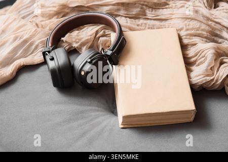 Wireless headphones and blank book on gray fabric with beige scarf, audio learning and relaxation Stock Photo