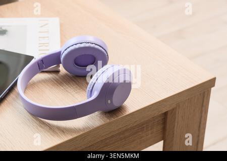Purple wireless headphones on wooden table with tablet and magazine, modern audio technology for music and podcasts Stock Photo