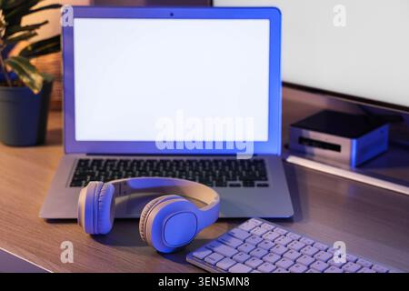 Modern home office setup with laptop, headphones, and keyboard on wooden desk for remote work and online learning Stock Photo