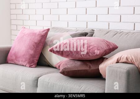 Comfortable gray sofa with assorted pink and geometric patterned throw pillows against white brick wall, the soft cushions provide a sense of relaxati Stock Photo