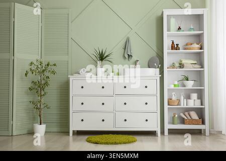 Modern bathroom interior design with white vanity, sink, and storage shelves against a green wall Stock Photo