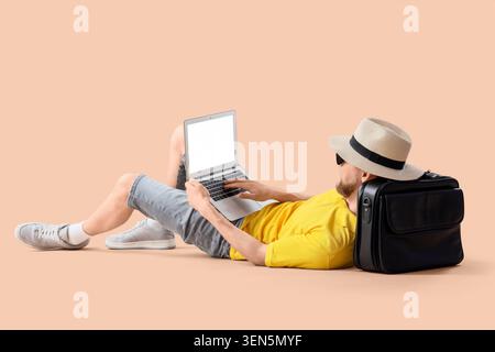 Young man in hat and sunglasses using laptop for remote work or online learning, relaxing on floor with briefcase Stock Photo