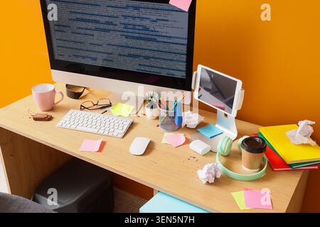 Messy programmer's desk with computer screen displaying code, tablet, coffee, and snacks on wooden table Stock Photo