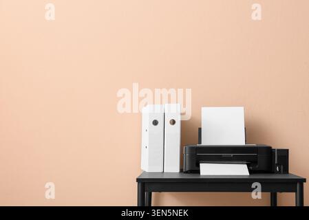 Modern home office setup with black printer, white paper, and document binders on a dark desk against a peach wall Stock Photo
