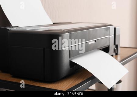 Modern black inkjet printer with white paper sheets on wooden desk, office equipment for printing documents and photos, sheet Stock Photo