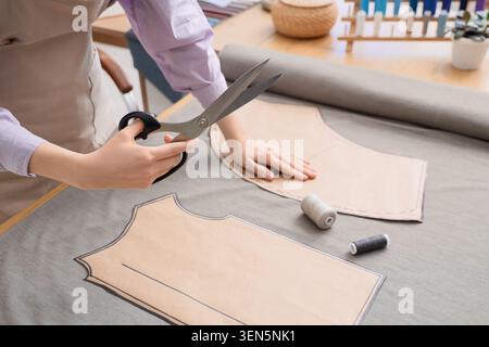 Fashion designer cutting fabric with scissors and paper pattern for garment creation and tailoring, the process involves careful tailoring and dressma Stock Photo
