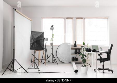 Professional photography studio setup with white backdrop, lighting equipment, and workspace for creative projects Stock Photo