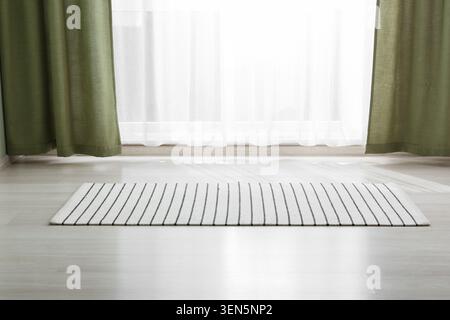 Modern home interior with striped area rug on light wood floor and green curtains by window, green curtains frame a bright window with sheer white dra Stock Photo