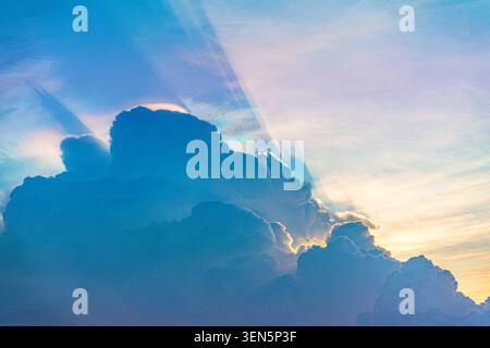 Dark thunderstorm cell with heavy rain and hail casts rays of sun and shadow, illuminated by the rays of the sunset in the iridescence and glow of cir Stock Photo