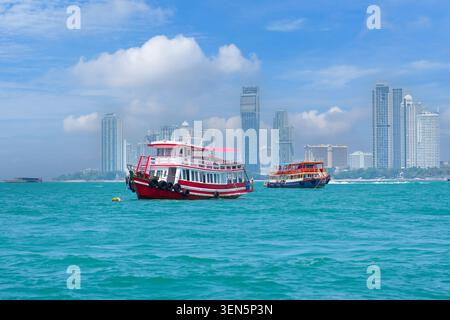 Two colorful boats float on turquoise waters with a modern city skyline in the background under a bright blue sky filled with fluffy clouds. Stock Photo