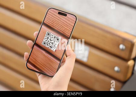 Hand holding smartphone scanning QR code on wooden bench, digital information access and contactless technology, the mobile device facilitates quick d Stock Photo