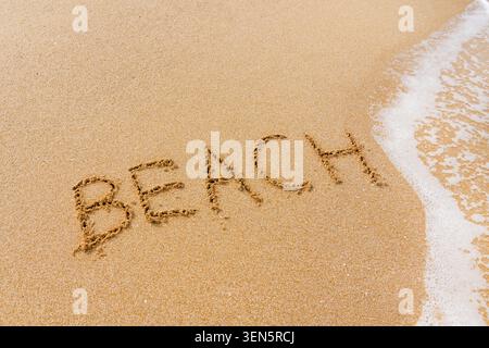 Word inscription on sand - Beach sand background with natural wave foam bubbles pattern. Stock Photo