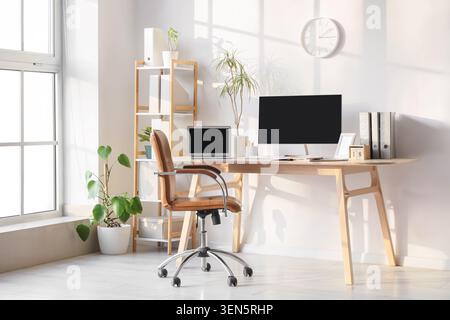 Modern home office workspace with computer, laptop, and desk chair in bright sunlight Stock Photo