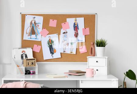 Fashion design studio workspace with cork board displaying stylish apparel sketches and creative tools Stock Photo