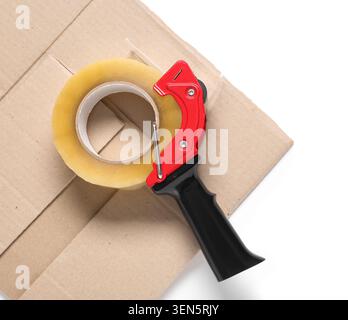 Red tape dispenser with clear packaging tape roll on brown cardboard box for shipping and moving Stock Photo