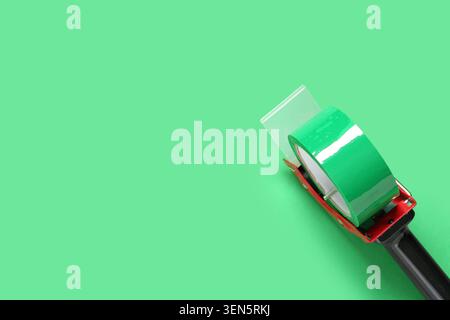 Green packaging tape dispenser with clear plastic blade on solid mint background for shipping and office supplies, this essential office and shipping Stock Photo