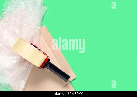 Shipping and packaging supplies with tape dispenser, bubble wrap, and cardboard on green background Stock Photo