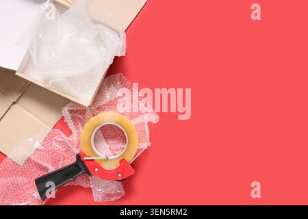 Cardboard box with bubble wrap and packing tape dispenser on red background for shipping and moving Stock Photo