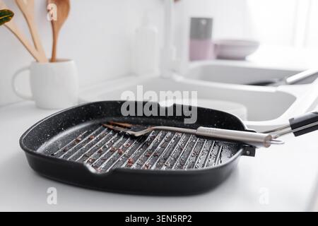 Dirty grill pan with spatula in kitchen sink, unwashed dishes and cooking utensils, household chores and cleaning Stock Photo