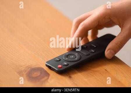 Hand operating smart home remote control for modern lighting system on wooden table, the black wireless device rests on a light wooden table, home aut Stock Photo