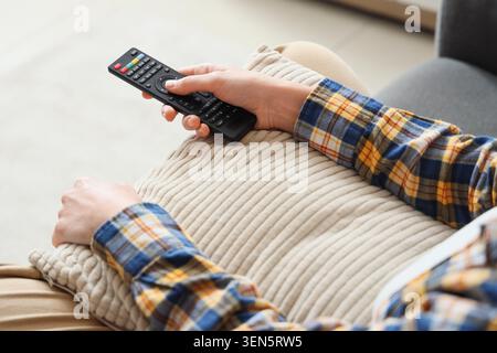 Relaxed person holding TV remote control on sofa, leisure and home entertainment, modern technology and comfort Stock Photo