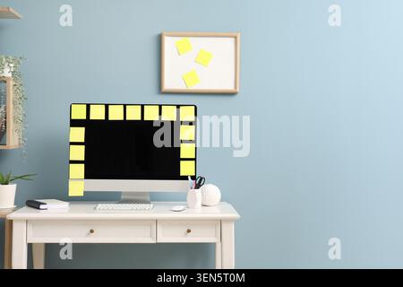 Home office desk with computer monitor and yellow sticky notes on light blue wall background Stock Photo