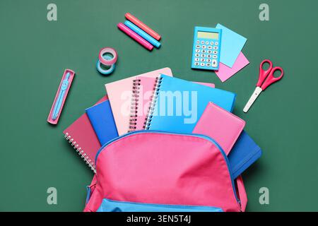 Pink and blue school backpack with assorted stationery items for education and learning on green background Stock Photo