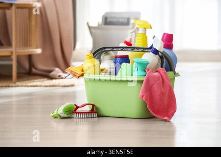 Household cleaning supplies in green plastic caddy with spray bottles and brushes on wooden floor, the caddy sits on a light wooden floor, ready for d Stock Photo