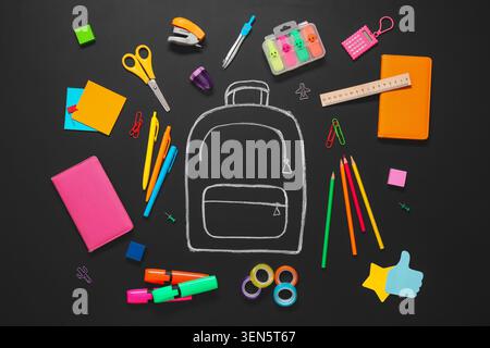 Back to school with chalk drawn backpack and colorful stationery on black chalkboard background, the items are neatly arranged on a black chalkboard b Stock Photo