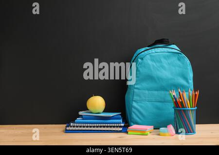 Back to school education with blue backpack, stack of notebooks, apple, and pencils on wooden desk Stock Photo