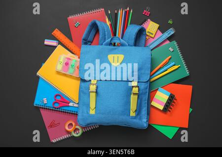 Blue school backpack with colorful school supplies and stationery for education and learning on black background Stock Photo