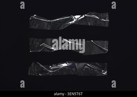 Three clear wrinkled plastic tape strips on black background, transparent adhesive texture overlay for design elements Stock Photo
