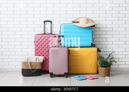 Colorful travel luggage stacked against white brick wall, vacation planning and holiday trip preparation Stock Photo