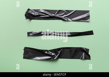 Three black duct tape strips on light green background, adhesive material for repair and craft projects, each piece of tape has a slightly wrinkled te Stock Photo