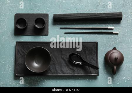 Asian cuisine dining set with black ceramic bowl, chopsticks, and teapot on textured blue background Stock Photo