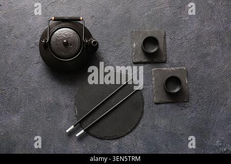 Traditional japanese cast iron teapot with chopsticks and slate coasters on dark textured background, the black teapot features a textured lid and han Stock Photo