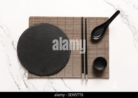 Asian cuisine dining set with black slate plate, chopsticks, spoon, and sauce bowl on bamboo mat Stock Photo