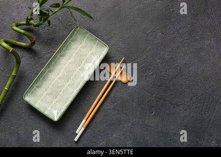 Asian cuisine dining set with green patterned plate, chopsticks, and lucky bamboo on dark textured background Stock Photo
