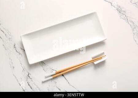 Empty white rectangular ceramic plate with wooden chopsticks on marble table, asian cuisine dining setup Stock Photo
