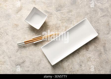 Empty white ceramic sushi plate and square sauce dish with chopsticks on textured concrete background, the rectangular plate and small square dish are Stock Photo