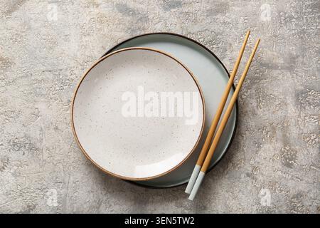 Empty ceramic plates and chopsticks on textured concrete background, asian cuisine dining utensils, the clean tableware is ready for an asian cuisine Stock Photo