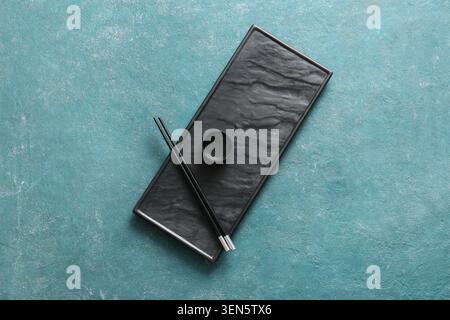 Empty black rectangular sushi plate with chopsticks and sauce dish on textured blue background, this setup is ready for an asian meal, providing a cle Stock Photo